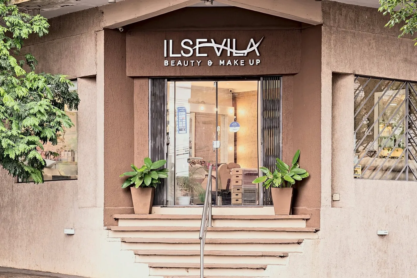 Entrada del salón Ilse Vila Beauty & Make Up, con el logo corpóreo, escalinata y plantas